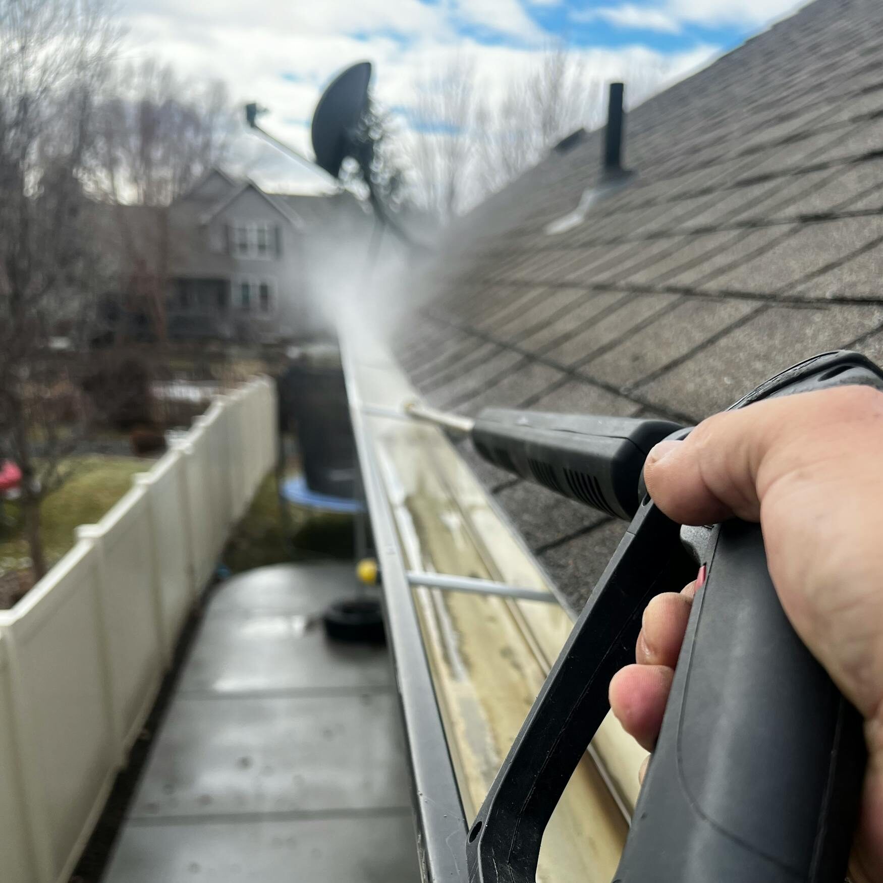 Close-up of gutter cleaning with pressure washer, outdoors, during the day.
